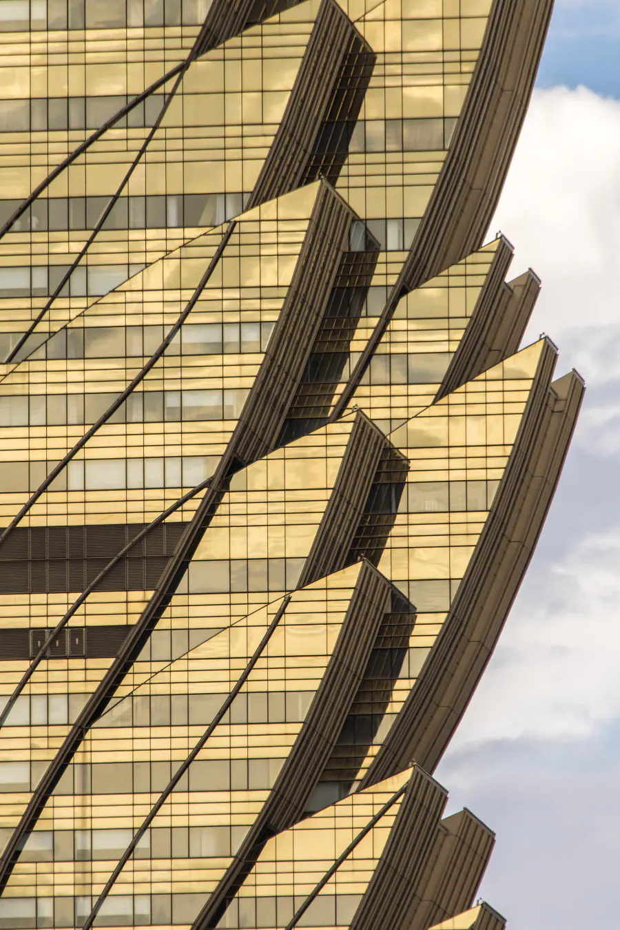 Close view of the Grand Lisboa's golden shell: overlapping curved petals of bronze glass peeling outward from the tower against a cloudy sky