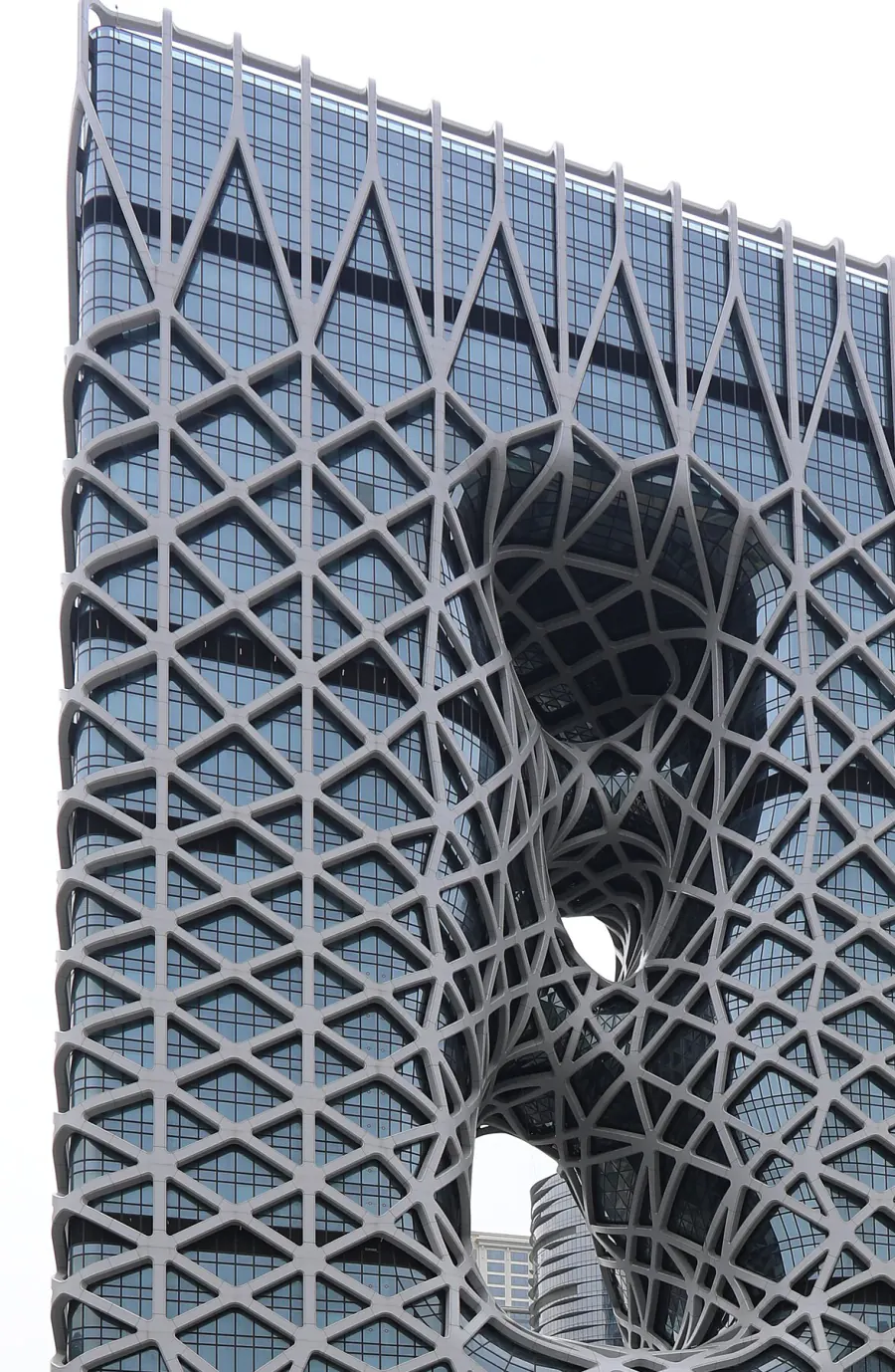 Close view of the Morpheus exoskeleton: a white steel net thickening around two voids punched clean through the tower, with the glass wall set behind it